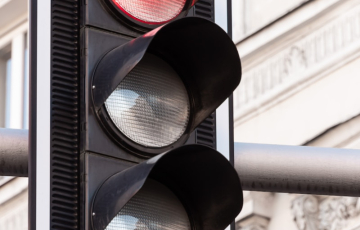 A traffic light showing a red signal, mounted on a pole, with a building in the blurred background.